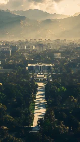 Sunlit boulevard slicing a misty mountain crowned cityscape.