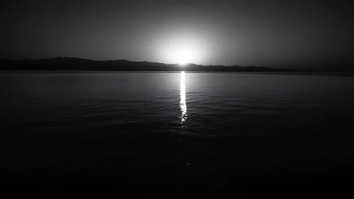 Black and white seascape captures sun setting behind ridge