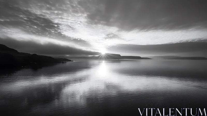 Monochrome coastal sunrise over calm reflective water.