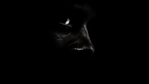 Glimmering face emerging gently from deep shadowed dark.