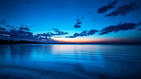 Blue seascape at dusk with calm water and clouds.