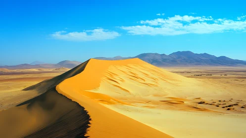 Crested desert sand dune under clear blue sky with mountains