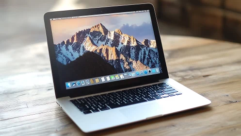 Open laptop on wooden table displaying mountain wallpaper.
