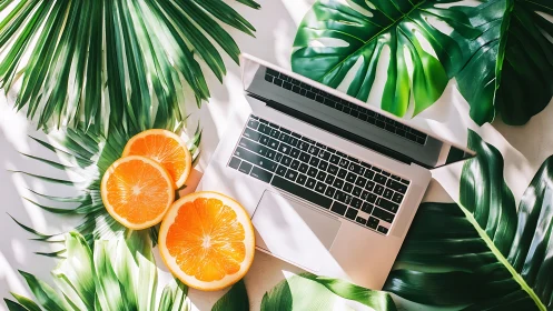 Laptop rests among tropical leaves and oranges in bright light