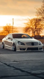 Sleek white coupe resting low under a gentle sunset sky.