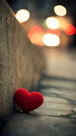 Red textile heart positioned against concrete base with bokeh lights.