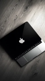 Closed black laptop with logo on grey wooden desk surface.