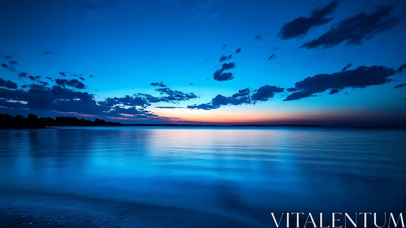 Blue seascape at dusk with calm water and clouds.