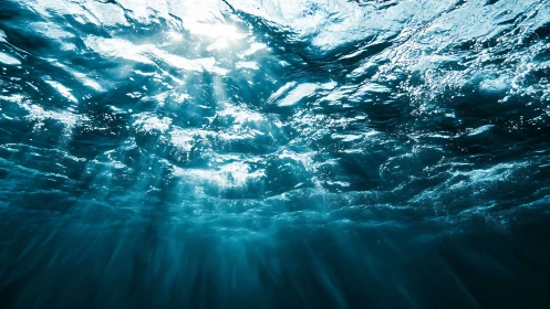 Sunlit underwater waves with radiant blue light beams.