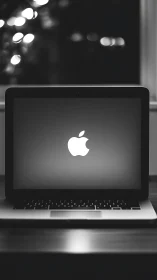 Apple laptop on desk in dark room with glowing screen.