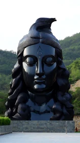 Monolithic black Shiva head statue in landscaped hillside plaza.