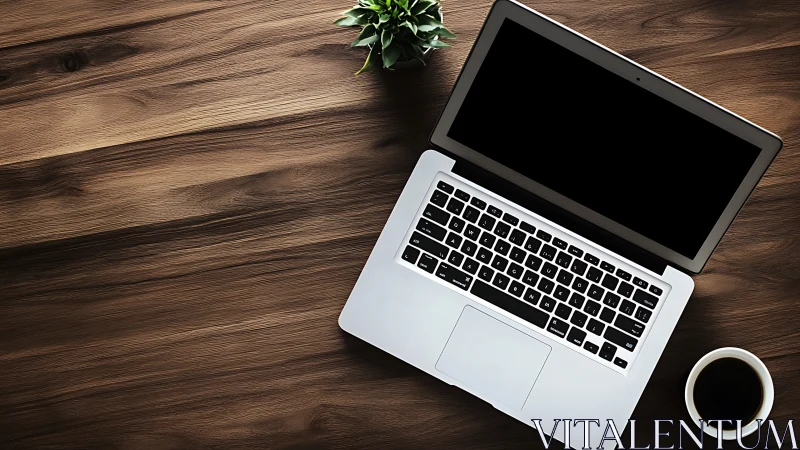 Overhead view of aluminum laptop on wood desk with coffee and plant