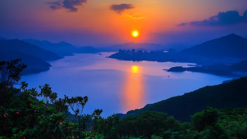 Coastal bay at sunset with distant city and layered hills.