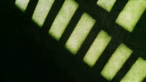 Abstract sunlight shadows on textured green fabric background.