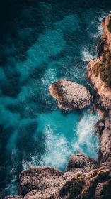 Turquoise surf crashing against sunlit coastal cliffs aerial.