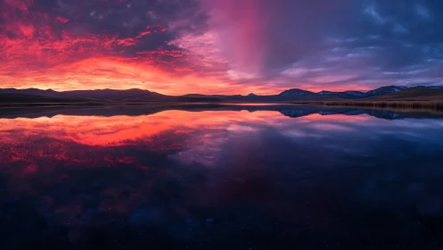 Panoramic mountain lake sunset with mirrored crimson sky.