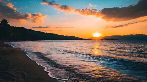 Sunset over coastal shoreline with distant hills and clouds.