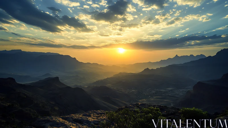 Sunset over layered mountain valley with scattered clouds.