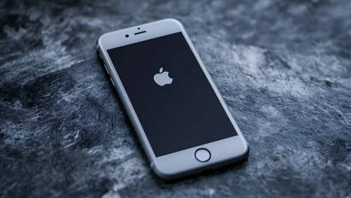 White iPhone displaying startup screen on textured stone surface