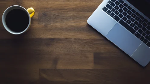 Overhead composition of laptop and coffee on laminated wood.