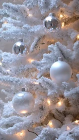 Snowy white Christmas tree glowing with soft silver baubles.