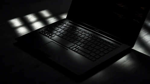 Sleek black laptop glows in dramatic low key lighting.