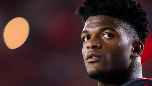 Focused football player gazes past glowing stadium lights.