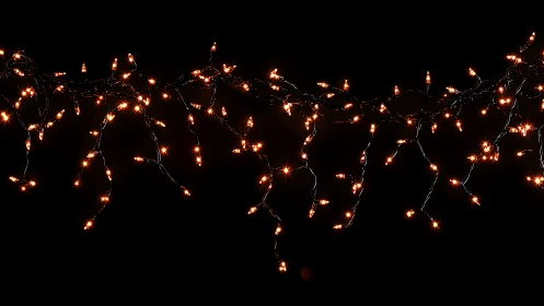 Warm amber icicle string lights suspended on black background.
