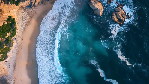 Aerial shoreline captures turquoise surf and sunlit rocks.