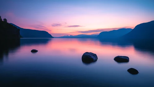 Serene mountain lake reflects pink and blue twilight glow.
