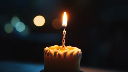 Lit Birthday Candle with Melting Wax Against Bokeh Background