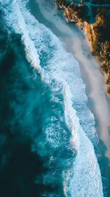 Aerial coastal shoreline with waves and sandy beach edge.