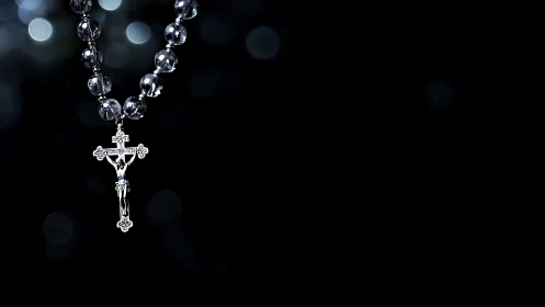 Silver crucifix rosary on black background, side lit.