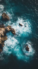Waves crash against coastal rocks in a vertical aerial view