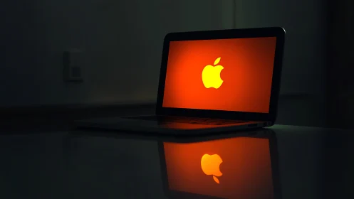Backlit laptop with glowing apple logo on red screen.