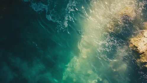 Sunlit turquoise shore with foaming waves and rock edge.