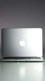 Closed silver laptop shows illuminated logo on desk