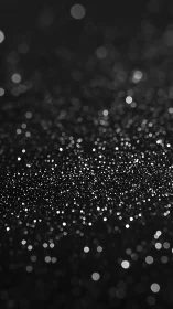Defocused black glitter surface with scattered light points.