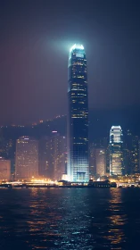 Skyscraper beacon rises above misty harbor skyline at night.