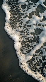 Foamy shoreline wave quietly dissolves over dark sand