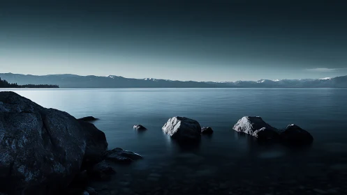 Nocturnal lakeside panorama with minimalist rock foreground.