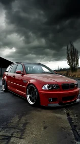 Red BMW wagon stands bold beneath threatening storm clouds.
