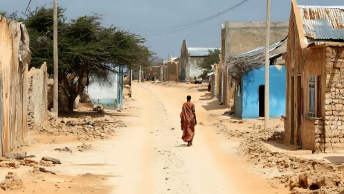 Solitary figure on sunlit sandy street in rural village.