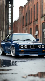 Restored blue BMW E30 coupe on wet industrial city street