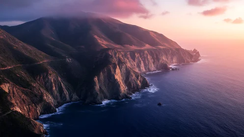 Sunset light over rugged ocean cliffs and coastal mountains.
