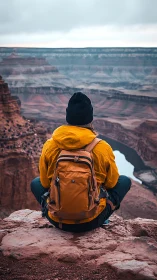 Solo hiker overlooks vast canyon under moody sky.