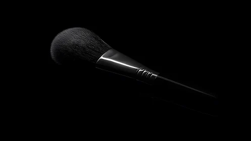 Elegant makeup brush in dramatic studio lighting on black background.