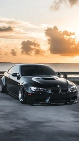 Lowered black BMW coupe dominates sunset coastal highway.