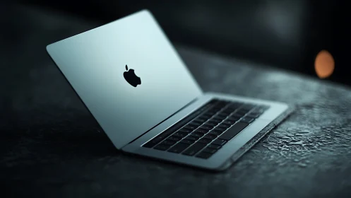 Sleek silver laptop rests on wet textured surface at night.