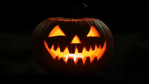 Grinning jack-o’-lantern glows with eerie Halloween light.